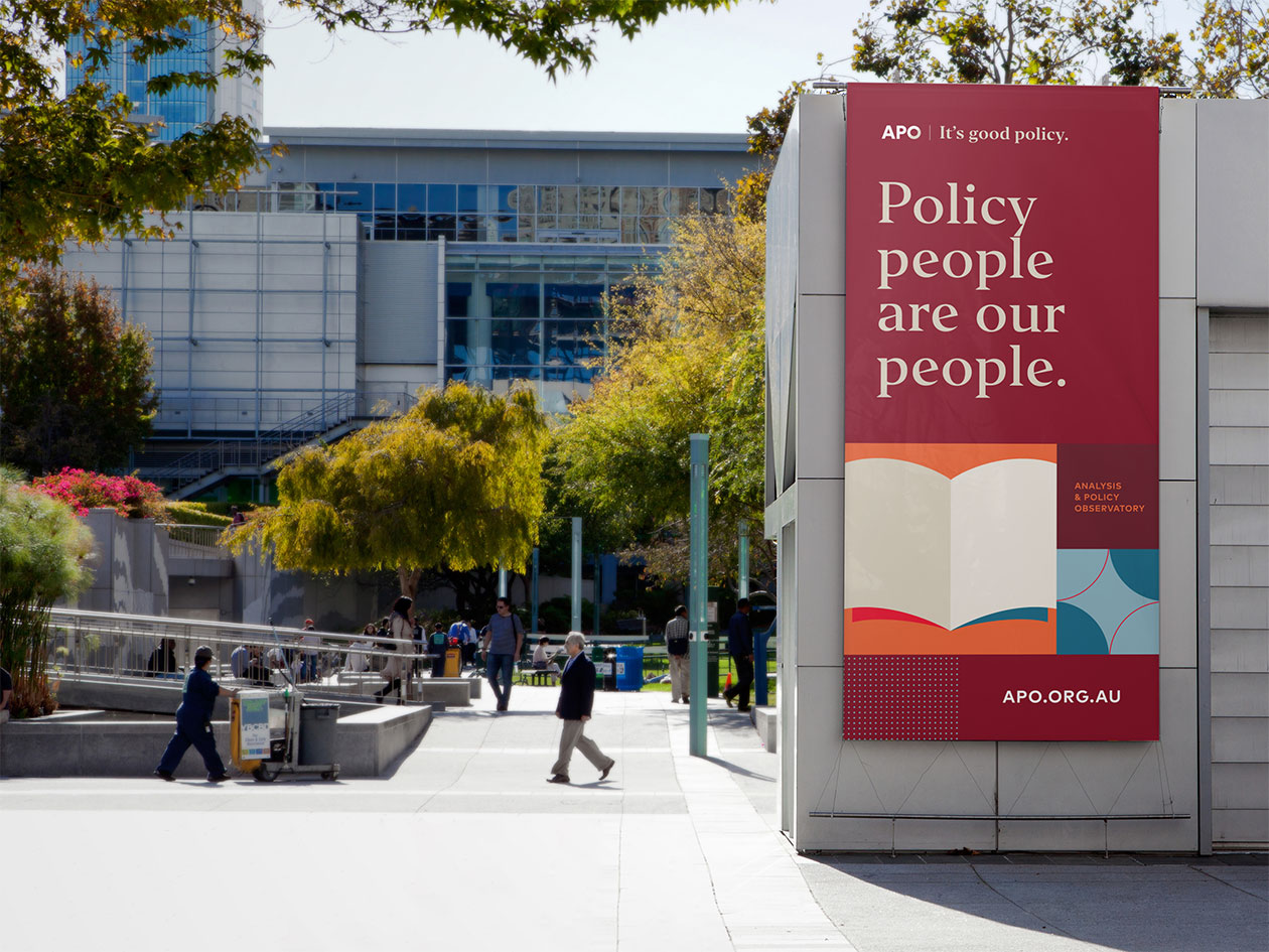 An external vertical hanging banner for APO with brand graphics and the headline "Policy people are our people".