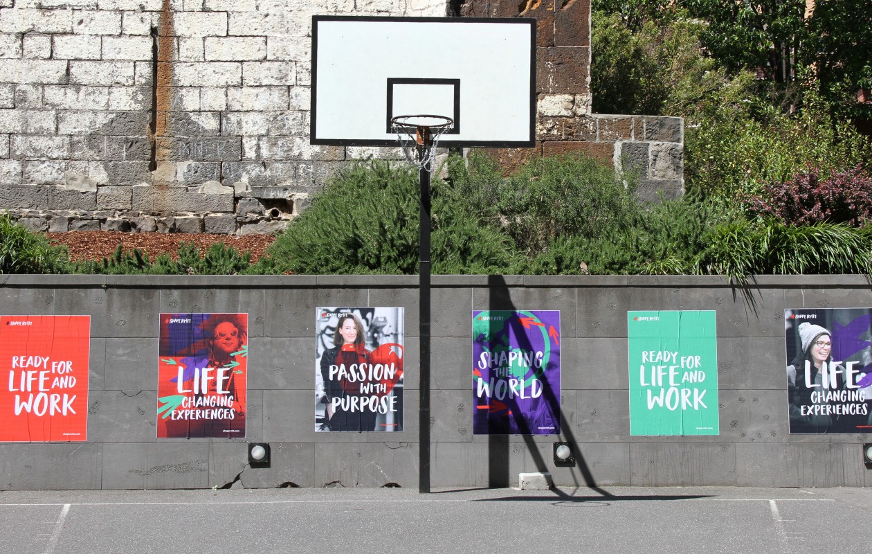 ShapeRMIT posters on a wall behind a campus basketball court