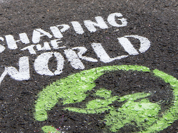 Chalk designs on an asphalt road with the tagline "Shaping the world" and an earth illustration.